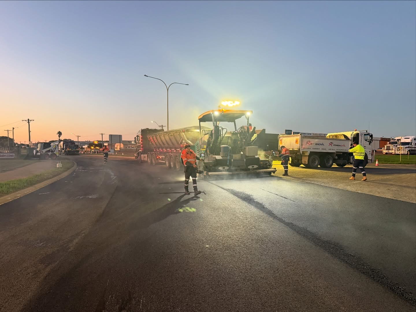 SuperCivil asphalt paver and crew laying fresh asphalt on a Western Australian road at dusk