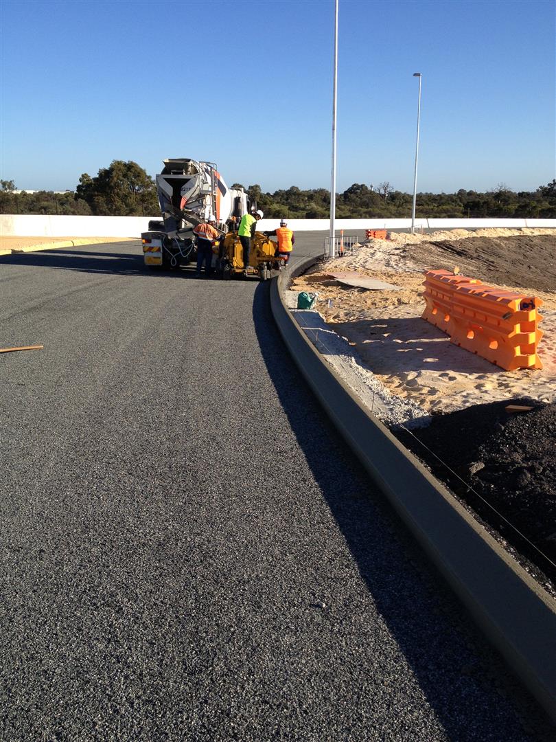 SuperCivil concrete kerbing machine and crew laying continuous kerbing along a freshly sealed road curve