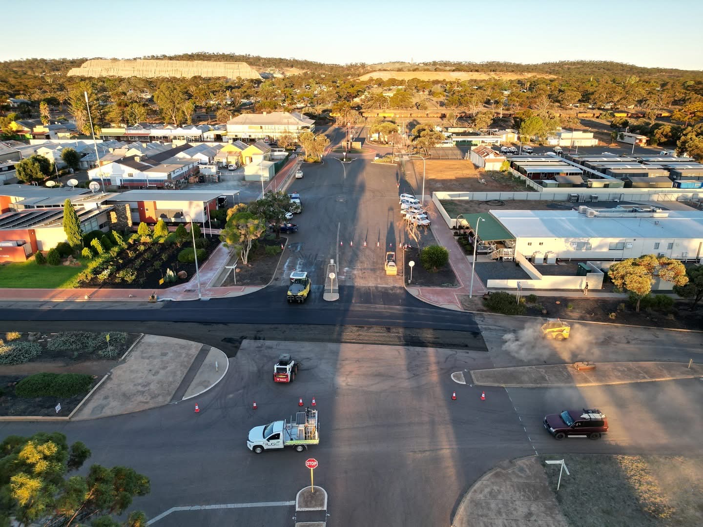 Aerial view of a regional Western Australian town intersection being resurfaced with fresh asphalt, a road roller, traffic management and SuperCivil crew at golden hour